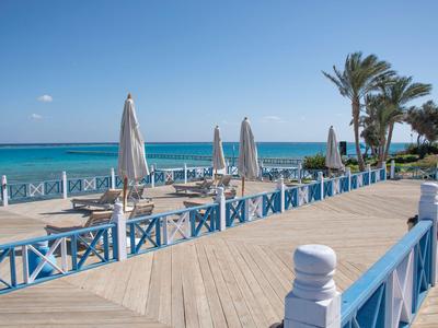 Holzpromenade mit blauen Geländern und Sonnenschirmen am Meer bei klarem Wetter.