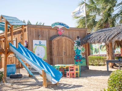 Plac zabaw dla dzieci z niebieską zjeżdżalnią, drewnianą konstrukcją i palmami na terenie hotelu.