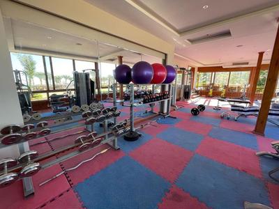 Fitnessraum mit buntem gepolstertem Boden, Hanteln, Gymnastikbällen und großen Fenstern mit Aussicht.