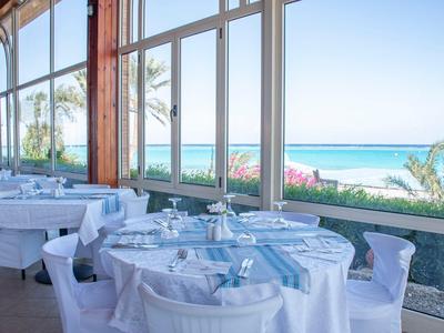 Elegantes Restaurant mit weißen Tischdecken und Blick auf das blaue Meer und Palmen.