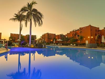 Basen hotelowy z palmami i budynkami o zachodzie słońca w tle.