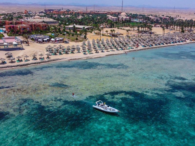 Przejrzysta turkusowa woda z łodzią przy szerokiej piaszczystej plaży i leżakami.