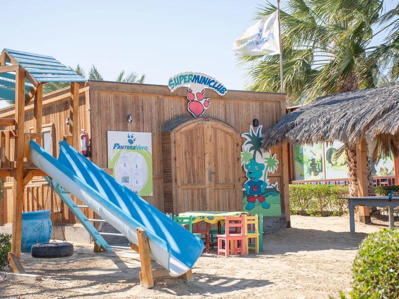 Plac zabaw dla dzieci z niebieską zjeżdżalnią, drewnianą konstrukcją i palmami na terenie hotelu.