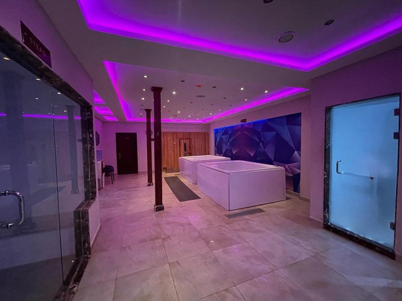 Nowoczesna strefa spa z jacuzzi, oświetleniem LED i szklanymi prysznicami.