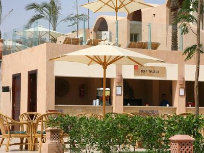 Area bar all'aperto con ombrellone, sedie e decorazioni tropicali in un resort.