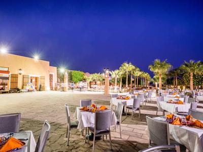 Area pranzo all'aperto serale con tavoli apparecchiati e palme sotto un cielo sereno.