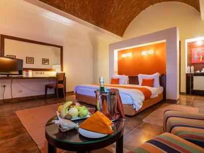 Camera d'hotel moderna con letto, scrivania e piatto di frutta su un tavolo.