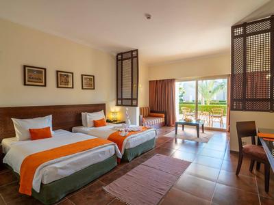 Camera d'hotel luminosa con due letti singoli, accenti arancioni e balcone con vista sul mare.