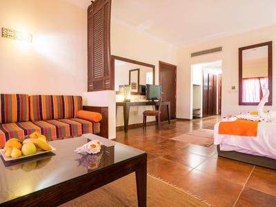 Camera d'hotel luminosa con divano, scrivania, letto, toni caldi e pavimento piastrellato.