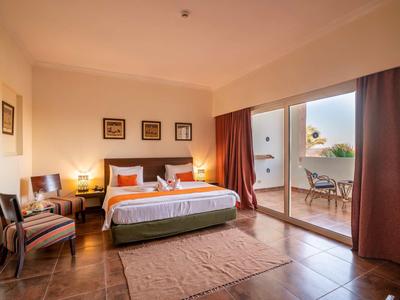 Camera d'hotel moderna con letto matrimoniale, poltrone, tappeto e terrazza alla luce del giorno.