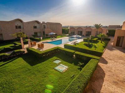 Complesso alberghiero con piscina, giardini curati e più edifici a due piani sotto il sole.