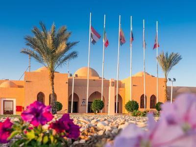 Edificio dell'hotel in tonalità sabbia calde con bandiere e palme sotto un cielo azzurro limpido