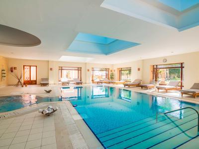 Ampia piscina coperta luminosa con più vasche e lettini nell'area relax.