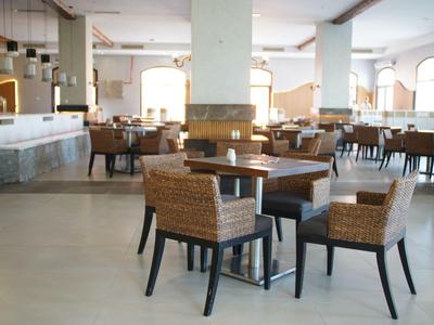 Ruime moderne hotel eetruimte met houten tafels en rotan stoelen bij daglicht.