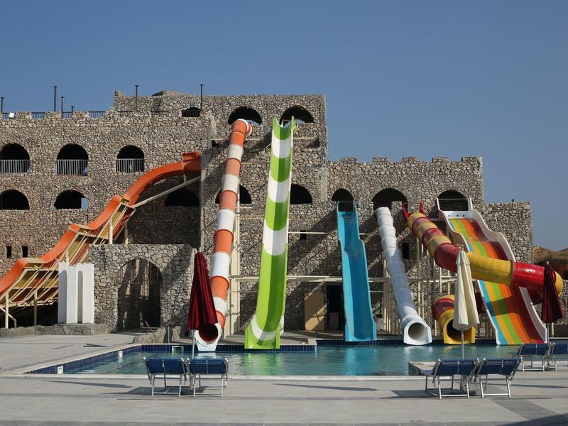 Gekleurde glijbanen voor een stenen gebouw en zwembad onder een heldere lucht.