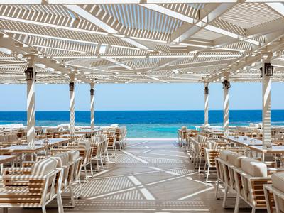 Area ristorante aperta con sedie e tavoli in legno con vista sul mare blu.