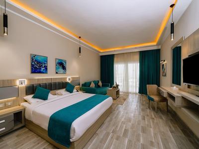 Chambre d'hôtel moderne avec lit king size, accents teal, canapé, bureau et grande TV.