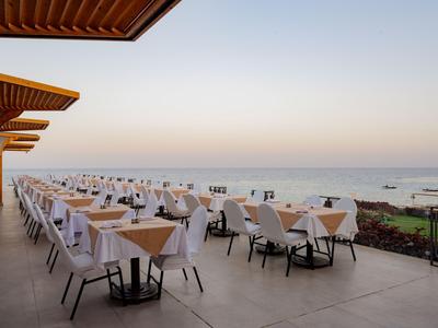 Terrazza del ristorante con tavoli apparecchiati e vista sul mare al tramonto.