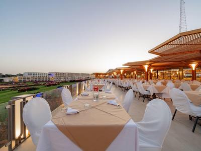 Terrasse de restaurant extérieure avec nappes blanches et chaises surplombant une pelouse verte et des bâtiments.