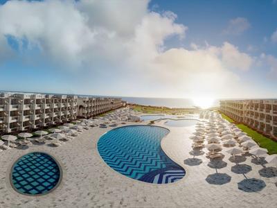 Moderno complesso alberghiero con piscina e ombrelloni al tramonto sulla spiaggia.