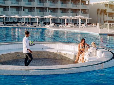 Piscina con una zona d'acqua circolare e due donne sedute sul bordo mentre un cameriere serve.