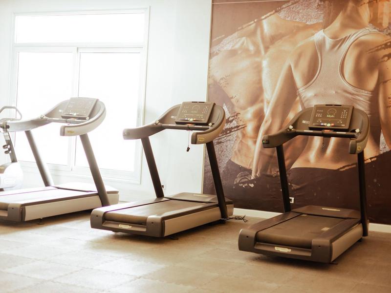 Trois tapis roulants dans une salle de sport lumineuse avec une grande affiche de fitness.