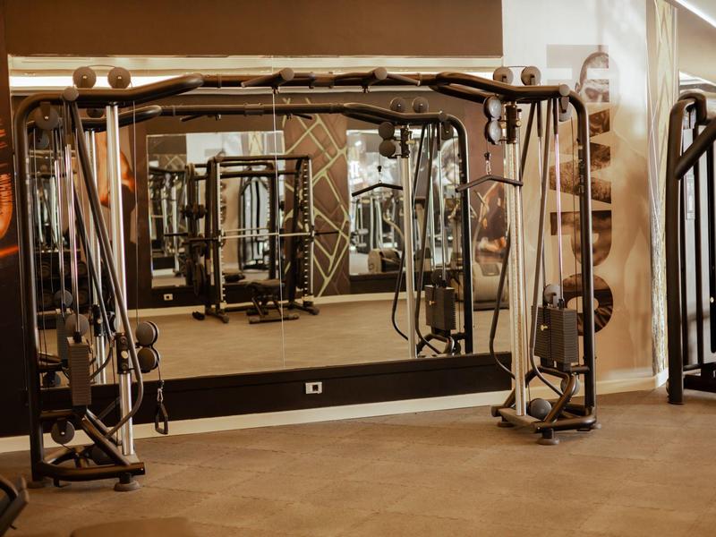 Salle de sport moderne avec appareils de musculation et grands miroirs sur un sol chaud.