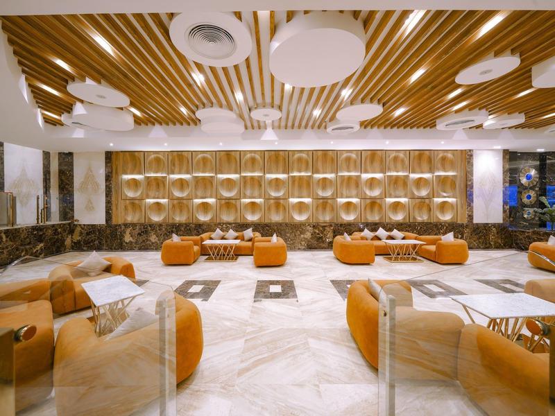 Hall d'hôtel moderne avec canapés orange, cloisons en verre et panneaux de plafond en bois.