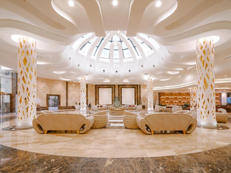 Hall d'hôtel luxueux avec piliers élégants, canapés circulaires et plafond éclairé par une verrière.