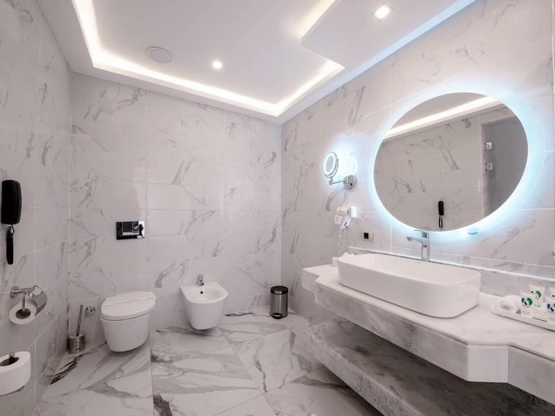 Salle de bain d'hôtel moderne avec murs en marbre, miroir rond éclairé et double lavabo.