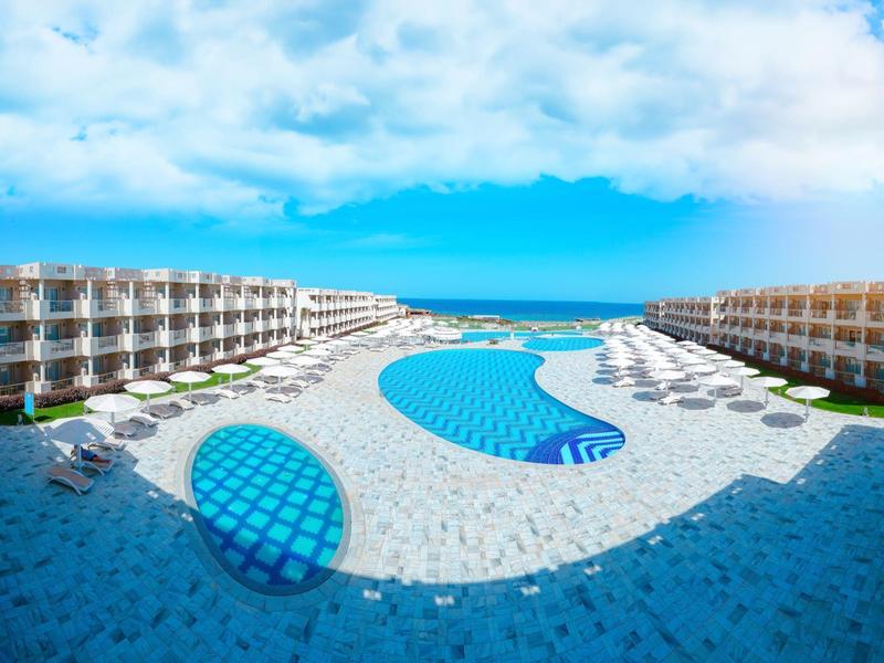 Hôtel moderne avec deux grandes piscines et des transats sous un ciel partiellement nuageux.