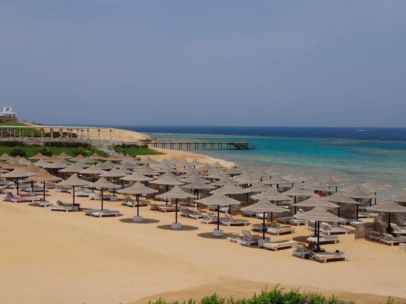 Plage de sable avec rangées de parasols et transats près d'une mer turquoise claire sous un ciel bleu.