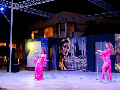 Dvě ženy v růžových kostýmech tančí na pódiu v noci s městským pozadím.