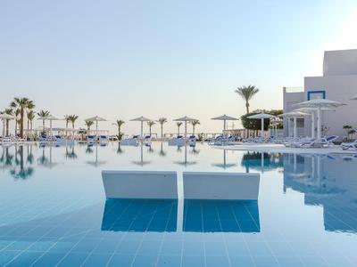 Infinity bazén s bílými lehátky, slunečníky a palmami pod jasnou oblohou v resortu