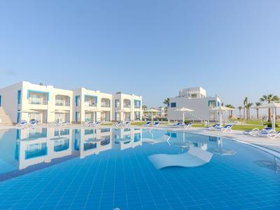 Velký modrý bazén před bílými hotelovými budovami se slunečníky a lehátky.