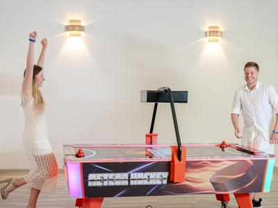 Dva lidé hrají air hockey u červeného stolu v jasně osvětlené místnosti.