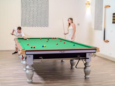 Dvě ženy hrají kulečník v moderní, světlé místnosti s dřevěnou podlahou.