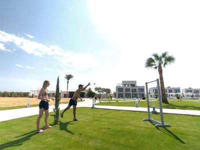 Tři lidé hrají volejbal na travnatém hřišti za slunečného počasí.