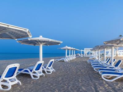 Pláž s modrými lehátky a slunečníky pod jasně modrou oblohou.