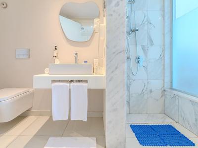 Světlá koupelna s toaletou, umyvadlem a sprchou s modrou podložkou.