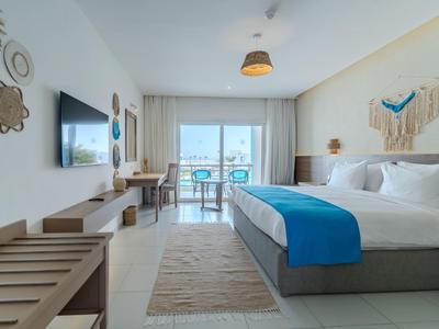 Moderní hotelový pokoj s velkou postelí, modrými akcenty a balkonem s výhledem na moře.