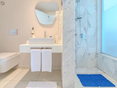 Moderní koupelna s toaletou, umyvadlem, velkým zrcadlem a sprchou obloženou mramorem.