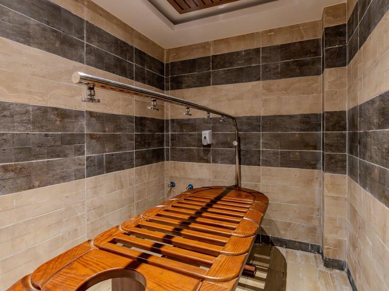 Dřevěné masážní lůžko v relaxační místnosti s kamennými obklady na stěnách.