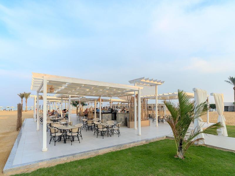 Otevřený venkovní prostor se stoly a židlemi pod bílou pergolou v hotelu.