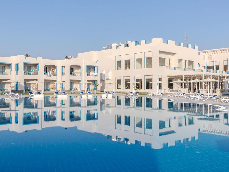 Moderní hotel s velkým bazénem a jasně modrou oblohou ráno.