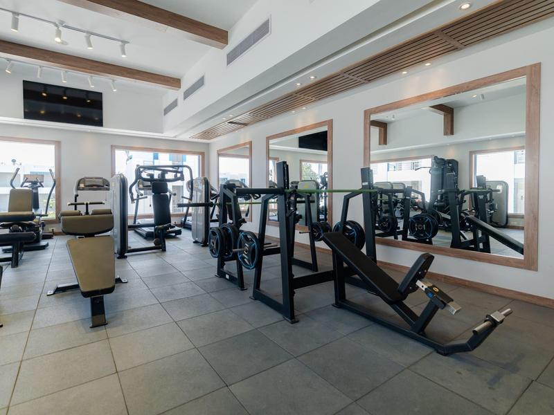 Světle vybavená posilovna s moderními přístroji a velkými zrcadly na stěně.