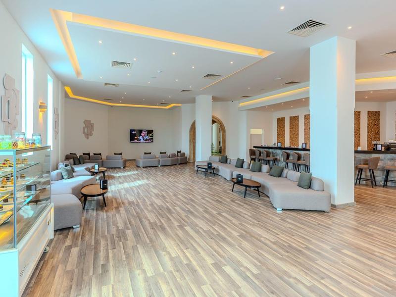 Světlá, moderní hotelová hala se sezením a pultem s pečivem.