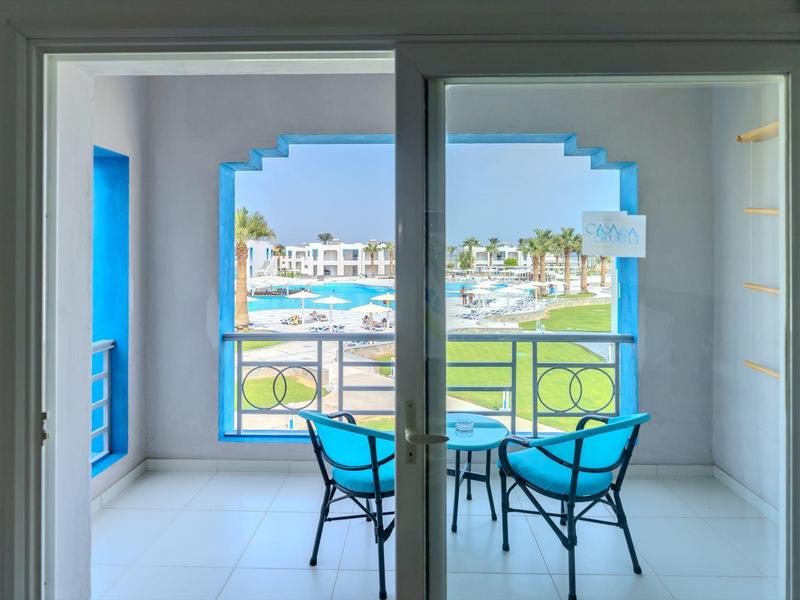 Balkon s modrými židlemi a stolem s výhledem na bazén a hotelové zařízení.