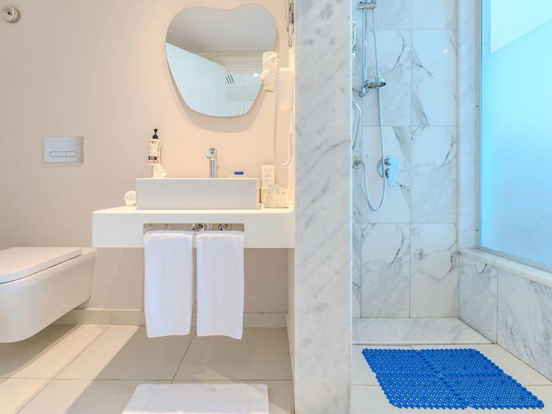 Světlá koupelna s toaletou, umyvadlem a sprchou s modrou podložkou.