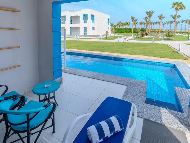 Výhled na bazén a zahradu z terasy s modrým lehátkem a židlemi.